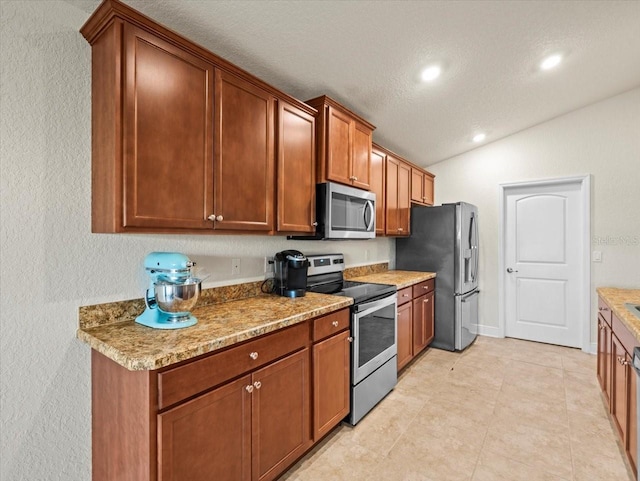 kitchen featuring appliances with stainless steel finishes, lofted ceiling, brown cabinets, and recessed lighting