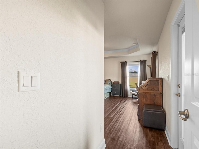 hall featuring dark wood-style floors, a textured wall, a raised ceiling, and ornamental molding