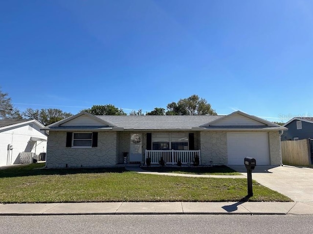 single story home featuring driveway, a garage, stone siding, covered porch, and a front yard