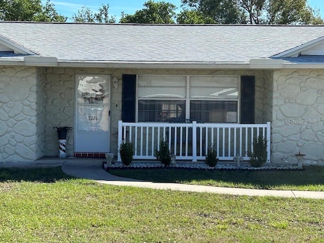 property entrance featuring stone siding, a yard, covered porch, and roof with shingles