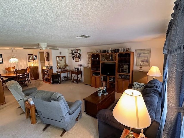 living area featuring visible vents, ceiling fan, a textured ceiling, and carpet flooring