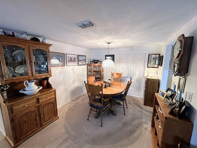 dining area with light colored carpet, visible vents, and a textured ceiling