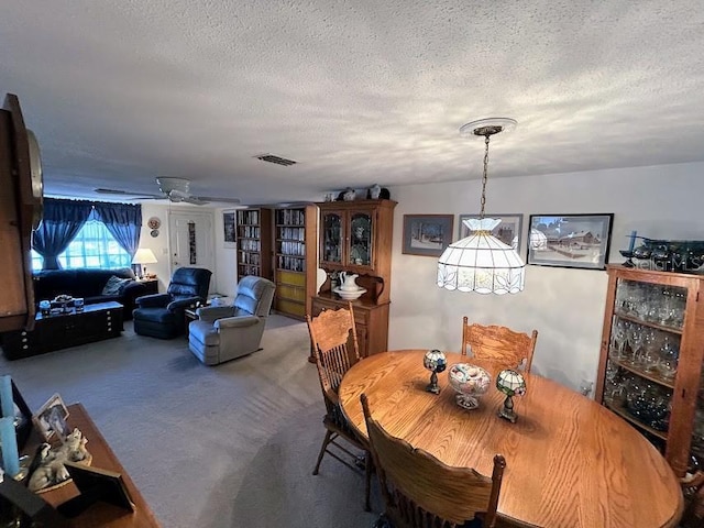 carpeted dining room with a textured ceiling, ceiling fan, and visible vents