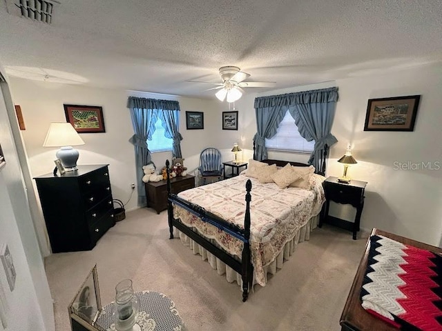 bedroom with a ceiling fan, light colored carpet, visible vents, and a textured ceiling