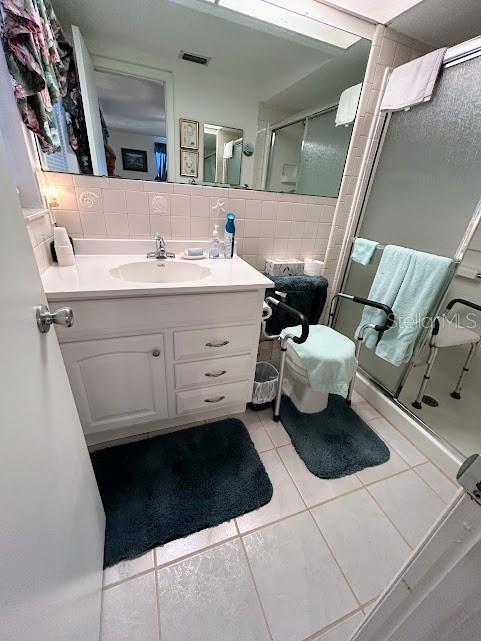 full bath with tile patterned flooring, vanity, visible vents, tile walls, and a shower stall