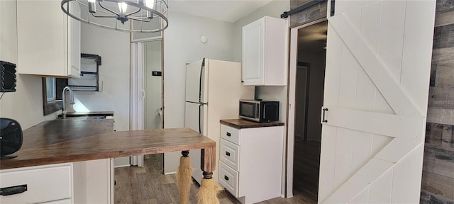 kitchen with a barn door, dark wood-type flooring, white cabinetry, wooden counters, and a sink