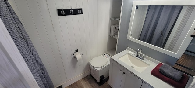 bathroom with toilet, wooden walls, wood finished floors, and vanity