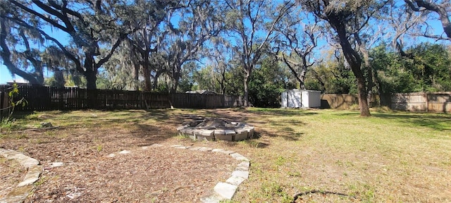 view of yard featuring a shed, a fire pit, a fenced backyard, and an outdoor structure