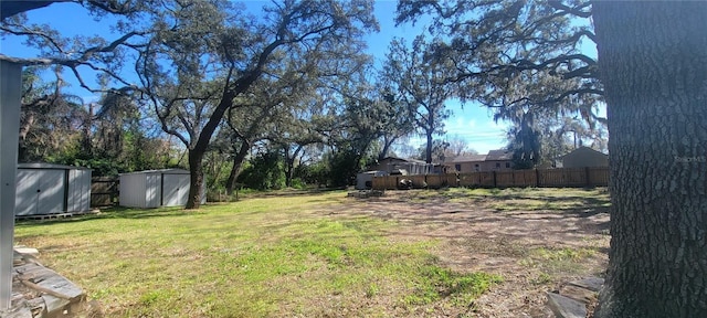 view of yard featuring fence, a storage unit, and an outbuilding