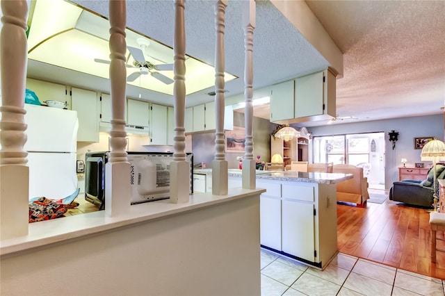 kitchen with light countertops, a ceiling fan, freestanding refrigerator, light tile patterned flooring, and a textured ceiling