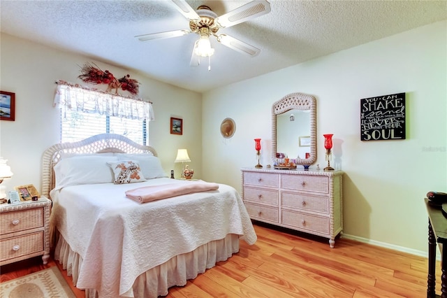 bedroom with light wood-type flooring, a ceiling fan, baseboards, and a textured ceiling