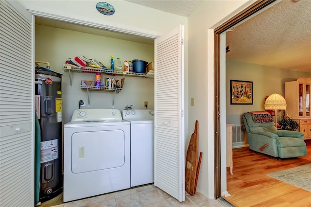 clothes washing area with laundry area, washer and clothes dryer, electric water heater, a textured ceiling, and light wood-style floors