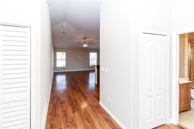 corridor featuring lofted ceiling, baseboards, and wood finished floors