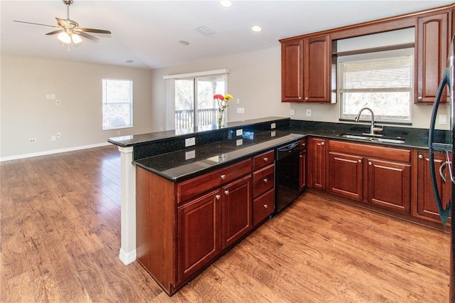 kitchen featuring dark stone counters, a peninsula, light wood-type flooring, black appliances, and a sink