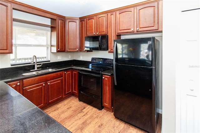 kitchen with dark stone counters, a sink, light wood finished floors, and black appliances