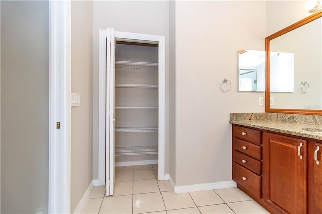 bathroom with baseboards, a walk in closet, vanity, and tile patterned floors