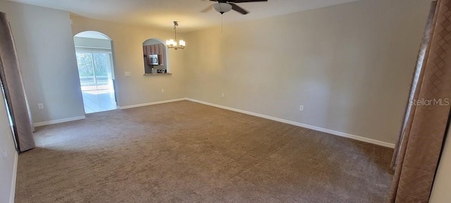 unfurnished room with arched walkways, dark colored carpet, ceiling fan with notable chandelier, and baseboards