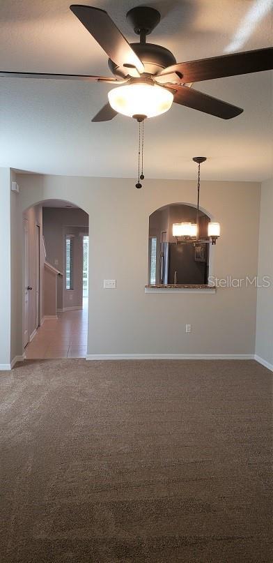 carpeted empty room featuring baseboards, arched walkways, a ceiling fan, and tile patterned floors