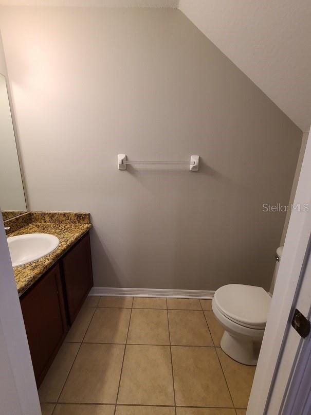 half bathroom featuring lofted ceiling, tile patterned flooring, toilet, vanity, and baseboards