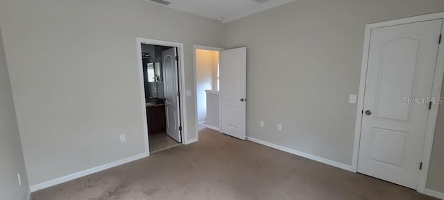 unfurnished bedroom featuring ensuite bath, light colored carpet, and baseboards