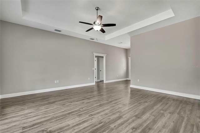 spare room with baseboards, a tray ceiling, ceiling fan, and wood finished floors