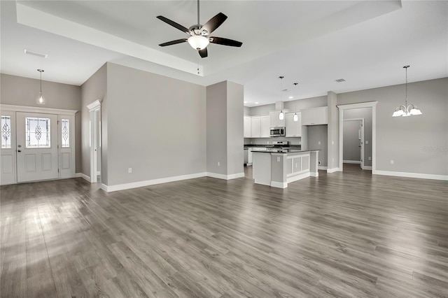 unfurnished living room featuring visible vents, baseboards, dark wood-style flooring, and ceiling fan with notable chandelier