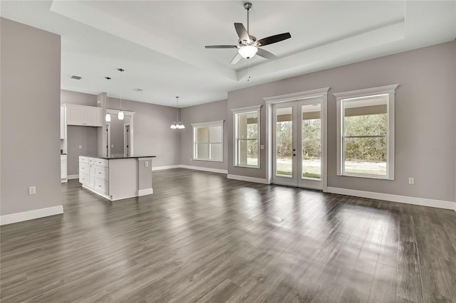 unfurnished living room featuring dark wood-style flooring, a raised ceiling, and baseboards