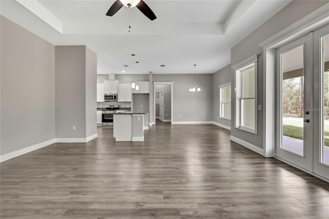 unfurnished living room with a tray ceiling, dark wood finished floors, baseboards, and ceiling fan with notable chandelier