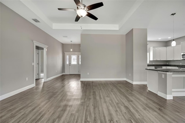 unfurnished living room featuring a raised ceiling, visible vents, a ceiling fan, wood finished floors, and baseboards