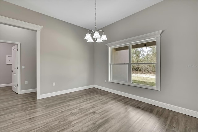 spare room with a notable chandelier, baseboards, and wood finished floors