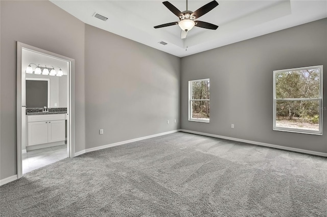 spare room featuring baseboards, a ceiling fan, light colored carpet, a tray ceiling, and a sink