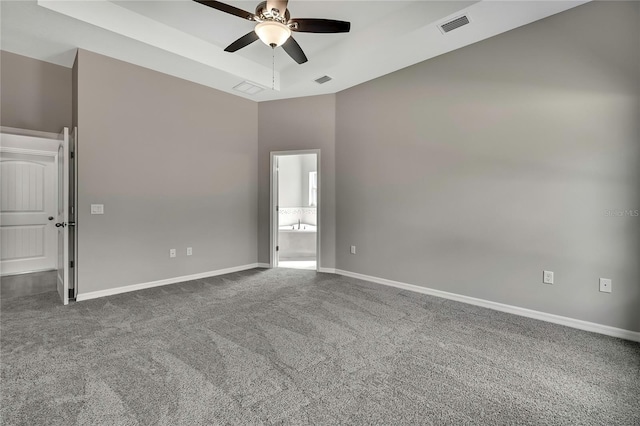 unfurnished room featuring baseboards, visible vents, a raised ceiling, ceiling fan, and dark carpet