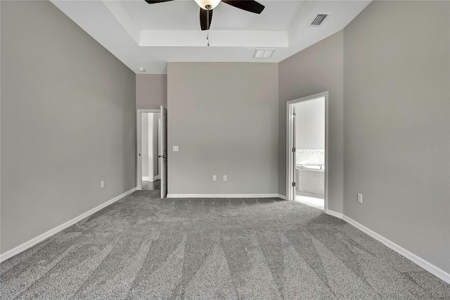 unfurnished bedroom featuring a tray ceiling, carpet flooring, visible vents, and baseboards