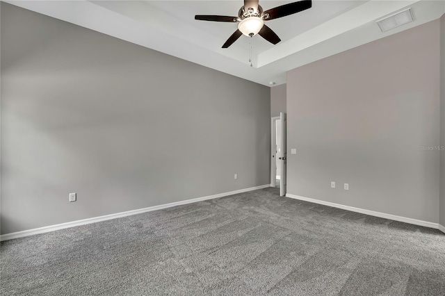 carpeted spare room featuring a raised ceiling, visible vents, ceiling fan, and baseboards