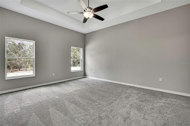 carpeted spare room with ceiling fan, a tray ceiling, and baseboards