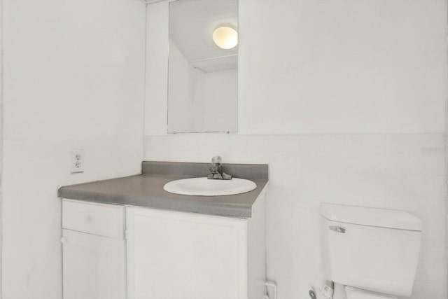 bathroom with toilet, a wainscoted wall, vanity, and tile walls