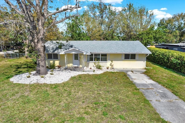 ranch-style house with a shingled roof, a front yard, and fence