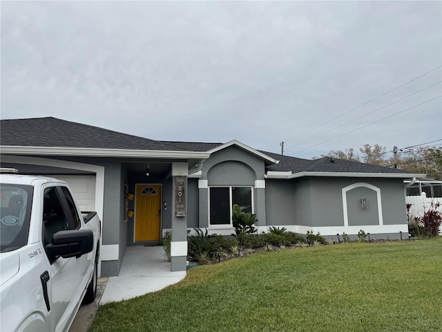 single story home with a shingled roof, a front yard, an attached garage, and stucco siding