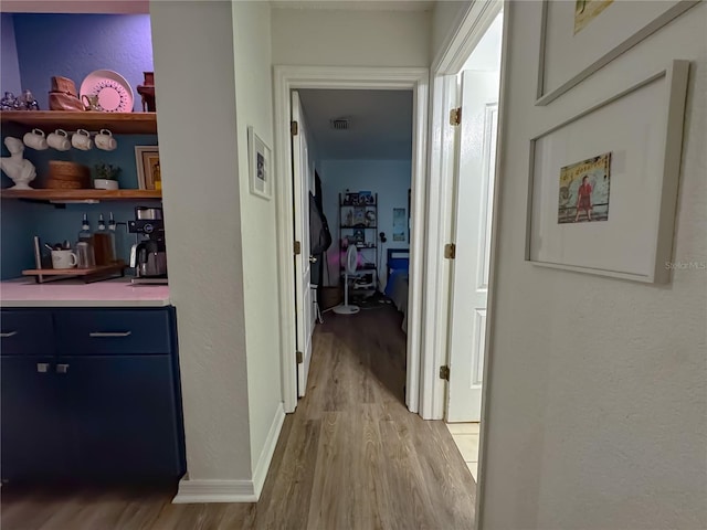 hall featuring visible vents, baseboards, light wood-style floors, and a textured wall