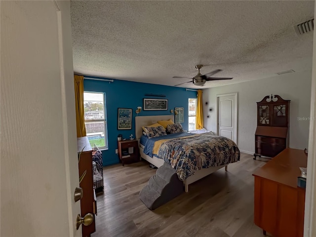 bedroom with visible vents, a textured ceiling, wood finished floors, and a ceiling fan