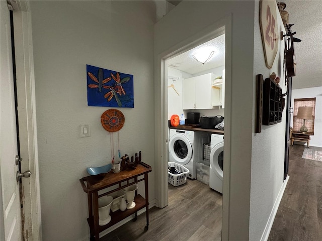 clothes washing area with a textured ceiling, cabinet space, wood finished floors, and washer and clothes dryer