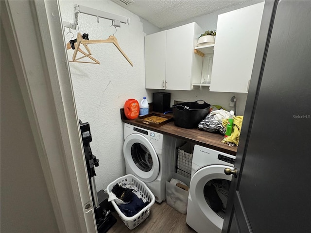 laundry area with cabinet space, a textured ceiling, wood finished floors, and washer and clothes dryer