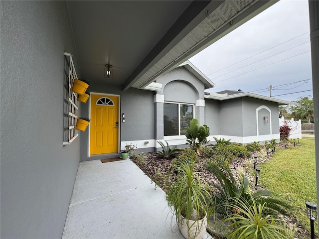 view of exterior entry featuring stucco siding and a lawn