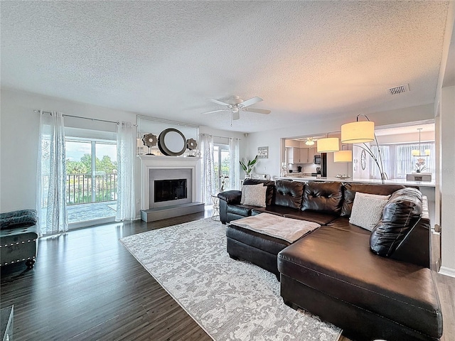 living area with a fireplace with raised hearth, a textured ceiling, wood finished floors, visible vents, and a ceiling fan