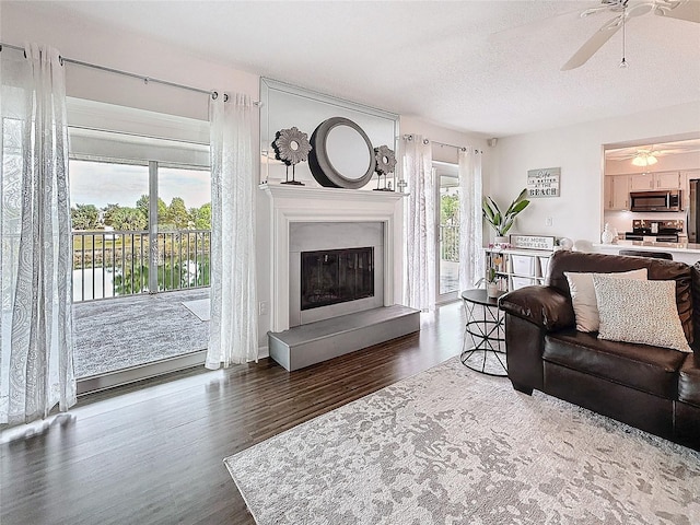 living area featuring ceiling fan, a textured ceiling, dark wood-style flooring, and a glass covered fireplace