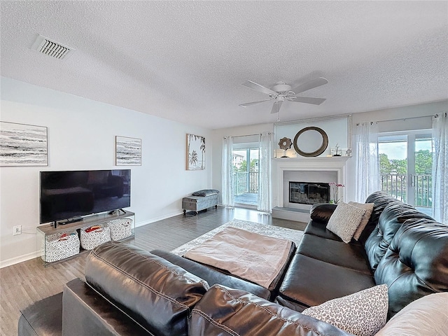 living area featuring visible vents, a glass covered fireplace, ceiling fan, a textured ceiling, and wood finished floors