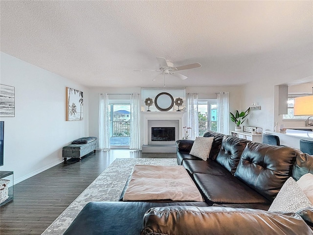 living room with baseboards, a glass covered fireplace, ceiling fan, dark wood-type flooring, and a textured ceiling