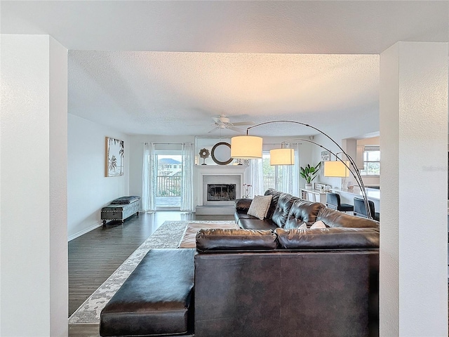 living area featuring plenty of natural light, a textured ceiling, dark wood-style flooring, and a glass covered fireplace