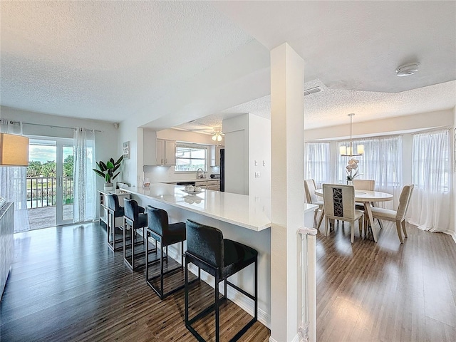 kitchen featuring a breakfast bar, dark wood-type flooring, a peninsula, light countertops, and pendant lighting