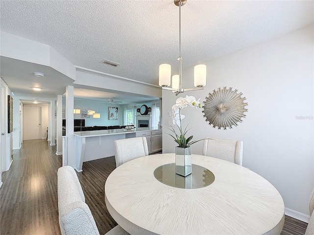 dining room featuring dark wood-type flooring, visible vents, a fireplace, and a textured ceiling